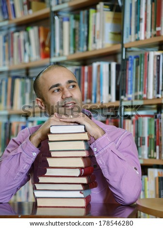 Portrait of male middle eastern student sitting at desk in Begen city library with a pile of books