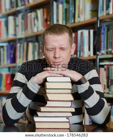 Portrait of male student sitting at desk in Begen city library with a pile of books and screwing up his eyes