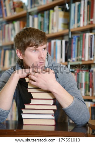 Portrait of male student sitting at desk in Bergen city library with a pile of books a