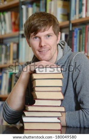 Portrait of male student sitting at desk in Bergen city library with a pile of books and looking at camera