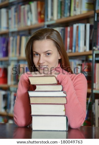 Portrait of beautiful student girl sitting at desk in Bergen city library with a pile of books and looking at camera