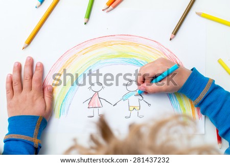 Close up of the hands of a little child drawing a happy family and a rainbow with color pencils