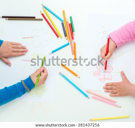Close up of the hands of little children drawing flowers with color pencils
