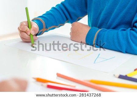 Close up of the hands of a little child drawing a flower with color pencils