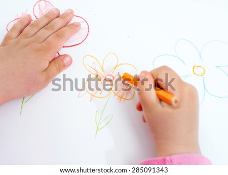 Close up of the hands of a little child drawing a flower with color pencils