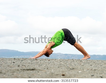 Young man practicing yoga on top of a mountain - downward dog pose