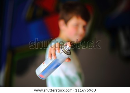 Boy pointing spray can. Focus on spray can with boy out of focus with graffiti in background.