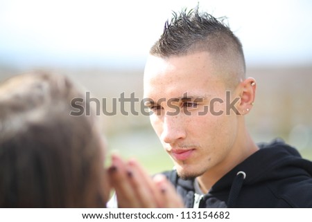 Young trendy urban couple in love. Good-looking man with Mohawk hairstyle and earrings, looking into his girlfriend\'s eyes. Hands pressed together.