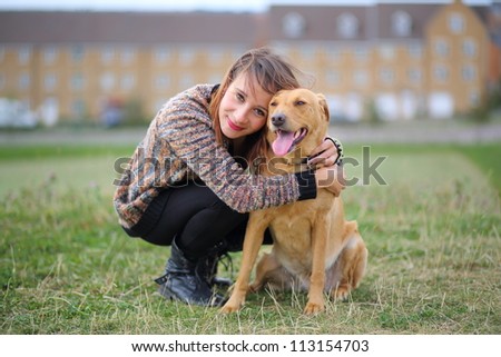 Pretty girl hugging Labrador dog. Suburban scene, in park with middle class housing in background.
