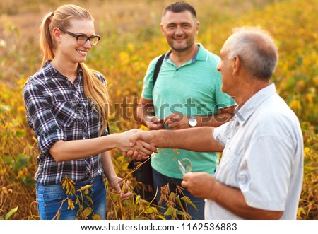 Handshake for deal, group of farmers standing in a field examining soybean crop before harvesting.