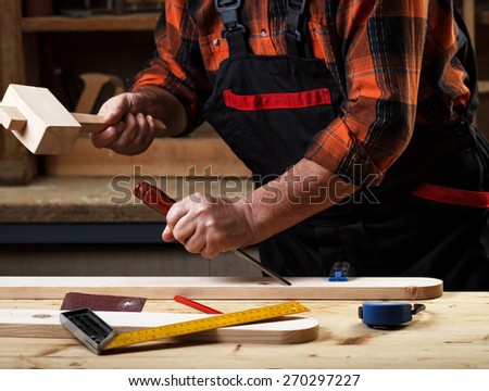 Senior carpenter working with a hammer, chisel and wood carving tools.