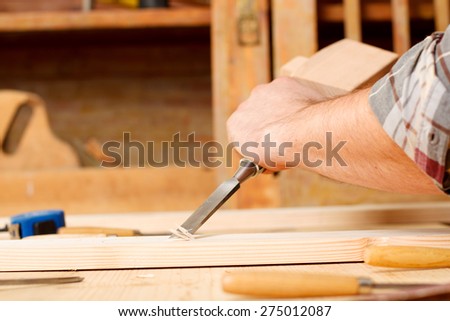 Closeup of a carpenter working with a hammer, chisel and wood carving tools.