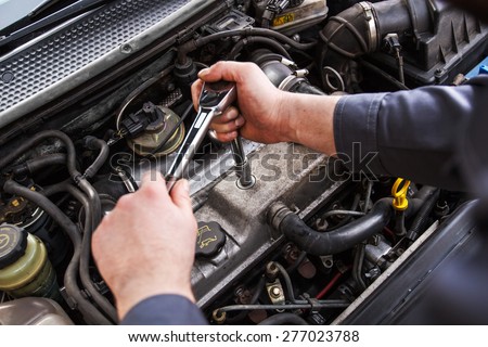 Mechanic working in a car under the hood, repairing an engine