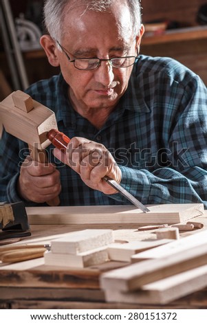 Closeup of a  senior carpenter working with a hammer, chisel and wood carving tools.