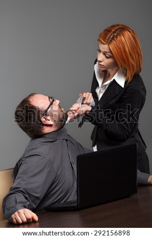 Businesswoman pulling a businessman for a necktie in office
