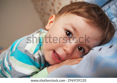 Little boy lying on the bed on his belly and looking at the camera, Natural light.