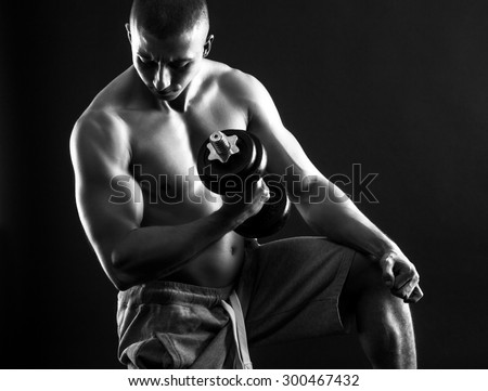 Young man with bare chest lifting dumbbells on black background. black and white