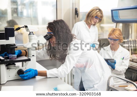 Photo of real female scientists looking into a microscope, photo taken behind the glass.