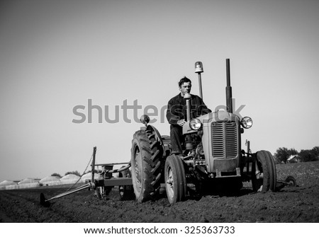 Farmer in Old-fashioned tractor sowing crops at field, black and white