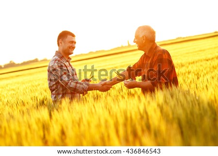 Two farmer standing in a wheat field and shake hands on sunset.