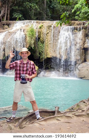 happy tourist with camera posing beside waterfall and green lagoon