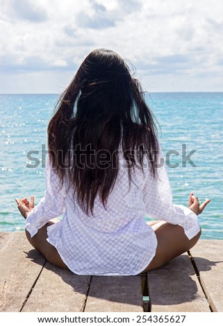back of woman in white shirt meditating by the sea