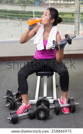 woman exercises with dumbbells and drinking a drink from a bottle at the gym