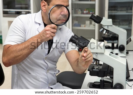 Man in the laboratory with microscope examines the sample under a magnifying glass