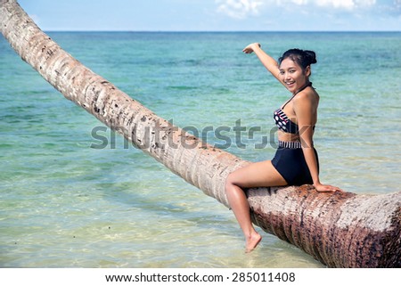 cheerful woman in retro swimsuit sitting on coconut palms and pointing to the sea