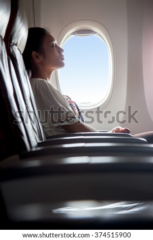 Woman sleeping in an airplane. Passenger in a flying aircraft sleep next to the window. Sleeping tired woman from a long airplane flight. Dreaming traveler on the plane beside a window with the blue.