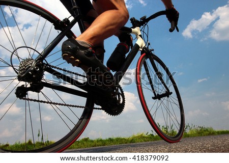 Close-up view on a cyclist on the road. Detail of a cyclist on bicycle. Road biker riding a bike on the road view from below. Cyclist rides on a background of blue summer sky.