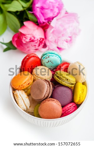 Colorful macaroons in a bowl with peonies on a white background
