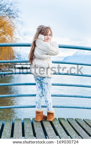 Outdoor portrait of a cute girl on a bridge on a nice winter day, wearing white jacket, printed jeans and brown boots