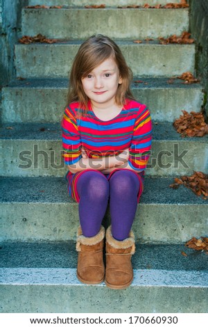Beautiful little girl sitting on steps outdoors, wearing colorful dress