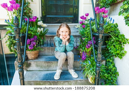 Outdoor portrait of a cute little girl sitting on steps in a city on a nice spring day