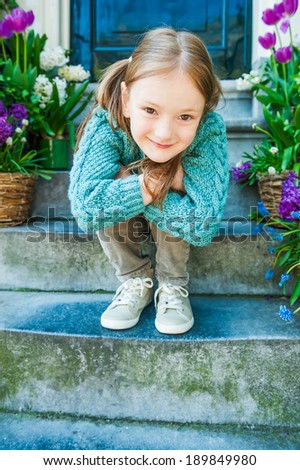 Outdoor portrait of a cute little girl sitting on steps in a city on a nice spring day