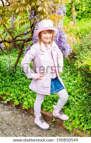 Spring portrait of a cute little girl, on a nice sunny day, wearing rain vinyl pink coat, hat and boots