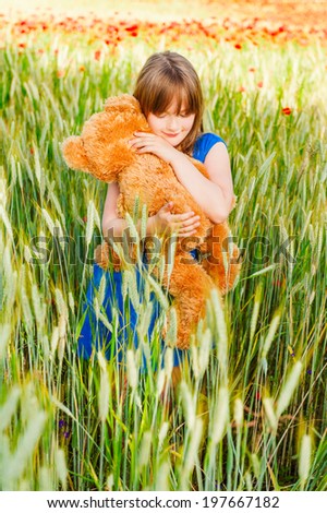 Summer portrait of a cute little girl playing with teddy bear in a wheat field