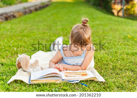 Portrait of adorable little girl resting outdoors and reading a book on a nice summer evening