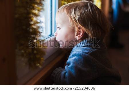 Cute toddler boy looking at the window at Christmas time