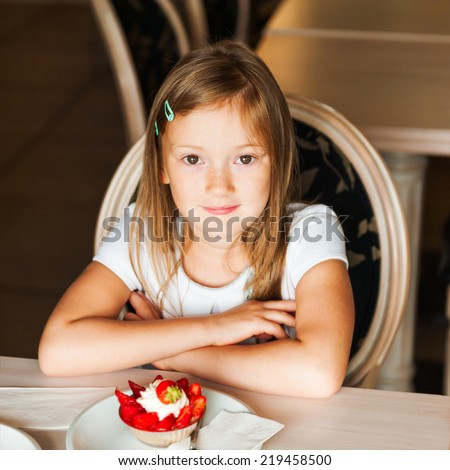 Cute little girl eating strawberry cake in a cafe