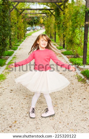 Cute little girl spinning around in a beautiful park, wearing tutu skirt, pink pullover and boots
