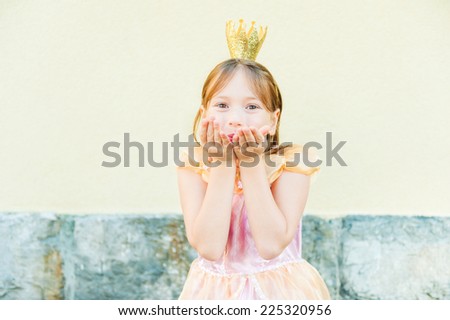 Cute little girl sending a kiss with her hands, weraring princess dress and a crown