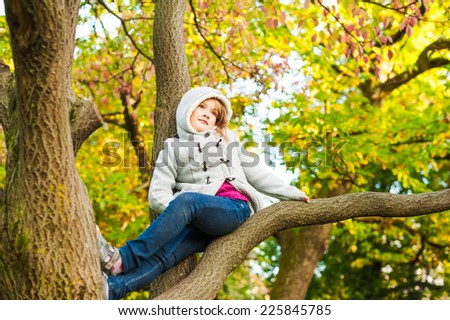 Autumn portrait of a cute little girl playing on a tree in a beautiful park on a nice sunny day
