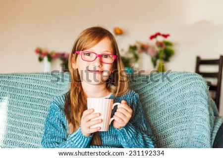 Indoor portrait of a cute little girl resting on a sofa with a cup of tea