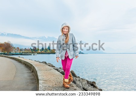 Cute little girl having fun outdoors, walking next to beautiful lake on a cold weather