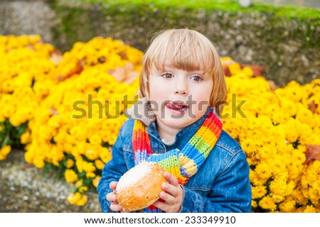 Cute toddler boy having snack outdoors, eating sugar bread