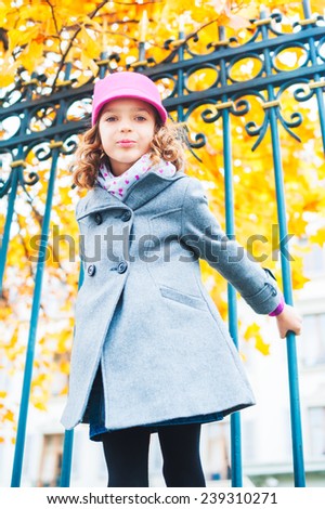 Lovely little girl playing outdoors, wearing grey coat and pink hat