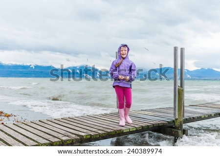 Adorable little girl feeding birds by the lake on a very windy day