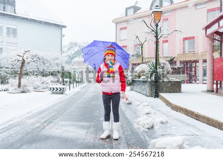 Outdoor portrait of a pretty little girl in a city under the snowfall